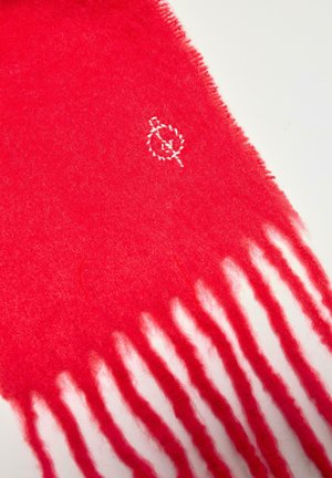 Sciarpa di lana rosso brillante con estremità frangiate e piccolo logo ricamato bianco vicino a un bordo su uno sfondo chiaro.