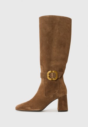 Botas de ante marrón hasta la rodilla con punta afilada, tacón cuadrado y un acento de hebilla dorada en el lado. Textura suave con un acabado mate.