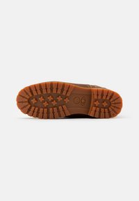 Semelle de chaussure brune avec un motif de traction détaillé. Matériau en caoutchouc orange, présentant des stries et des étoiles pour l'adhérence et la durabilité.