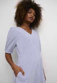 Striped dress in light blue and white. Features a V-neck, short puff sleeves, side pockets, and soft fabric texture.