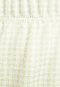 Tecido gingham verde-claro e branco com uma textura suave. O padrão apresenta pequenos quadrados, com um acabamento ligeiramente texturizado.