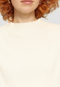 Rippstrick-Cremepullover mit hohem, rundem Ausschnitt. Weiche Textur mit taillierter Silhouette, die einen dezenten Glanz im Material zeigt.