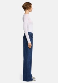 Top bianco a maniche lunghe abbinato a jeans blu a vita alta e gamba larga. I jeans presentano una classica trama in denim con tasche posteriori e cuciture chiare.