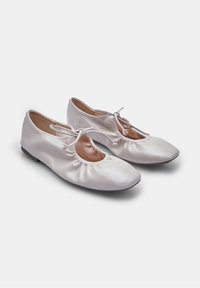 Valkoiset ballerinakengät, jotka on valmistettu sileästä nahasta, mukana pyöreä kärki, elastinen avaus ja kerrostettu muotoilu nilkan ympärillä.