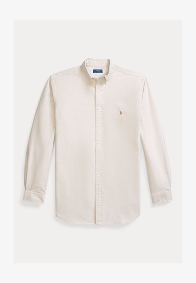 Langermet skjorte med knapper i kremfarget bomullsstoff. Har spredt krage og en liten brodert logo på brystet. Klassisk passform.