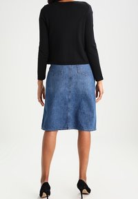 Top negro de manga larga combinado con una falda de mezclilla azul hasta la rodilla con bolsillos traseros y una silueta recta, usada con tacones negros.