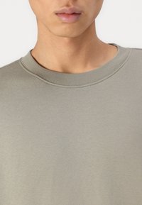 Sweatshirt vert clair présentant un col ras du cou et une texture douce. Le tissu présente un motif subtil et a des coutures visibles au niveau du col.