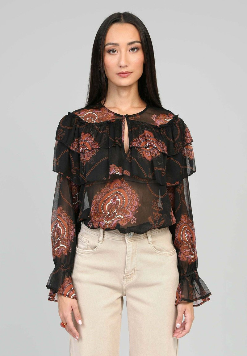 Blouse noire transparente avec des volants, motifs floraux en bordeaux et rose, accentuée d'un décolleté en trou de serrure et de poignets à manches évasées.