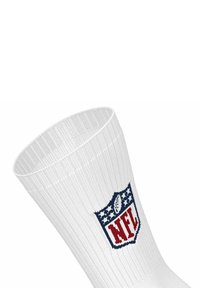 Calcetín deportivo blanco con textura acanalada y un logo de la NFL bordado en azul marino y rojo, con estrellas y rayas encima del logo.