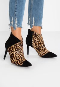 Botas de mujer de altura de tobillo con estampado de leopardo y acentos de ante negro, combinadas con jeans azules de dobladillo desflecado.