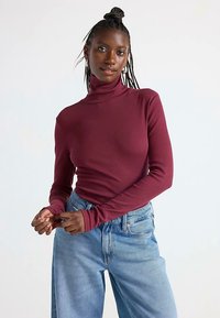 Viininpunainen ribbineulottu poolopaita pitkillä hihoilla, yhdistetty vaaleansinisiin korkeavyötäröisiin farkkuihin. Kangas näyttää pehmeältä ja vartalonmyötäiseltä.