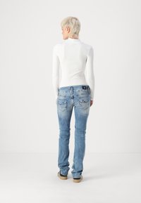 Light blue, slim-fit jeans with faded detailing and two back pockets, paired with a white ribbed long-sleeve top.