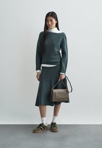 Pull tricoté bleu sarcelle foncé et jupe assortie, col roulé blanc en dessous, baskets vertes et sac bandoulière marron. Textures lisses.