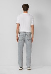 Biała koszulka z krótkim rękawem w zestawieniu z jasnoszarymi, prostymi spodniami dżinsowymi. Widoczne tylne kieszenie oraz minimalistyczny design. Całość dopełniają casualowe buty.