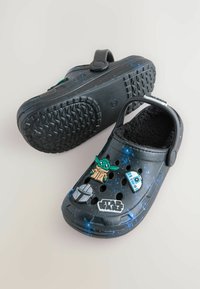 Zwarte Crocs met een kosmisch patroon, gemaakt van rubbermateriaal, met een fuzzy interieur en vier decoratieve Star Wars-thema bedels op de voorkant.