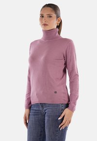 Maglione a collo alto rosa realizzato in un tessuto morbido, dal design aderente con maniche lunghe, con un piccolo dettaglio del logo in basso a sinistra.