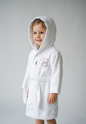Kleinkind lächelt, trägt einen weißen Kapuzenbademantel mit einer Teddybär-Stickerei auf der Brust und einem gebundenen Gürtel.