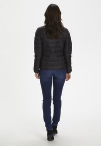 Svart isolerad jacka med horisontell quiltad mönster, långa ärmar och figurnära design, kombinerad med mörka denimjeans och svarta kängor.
