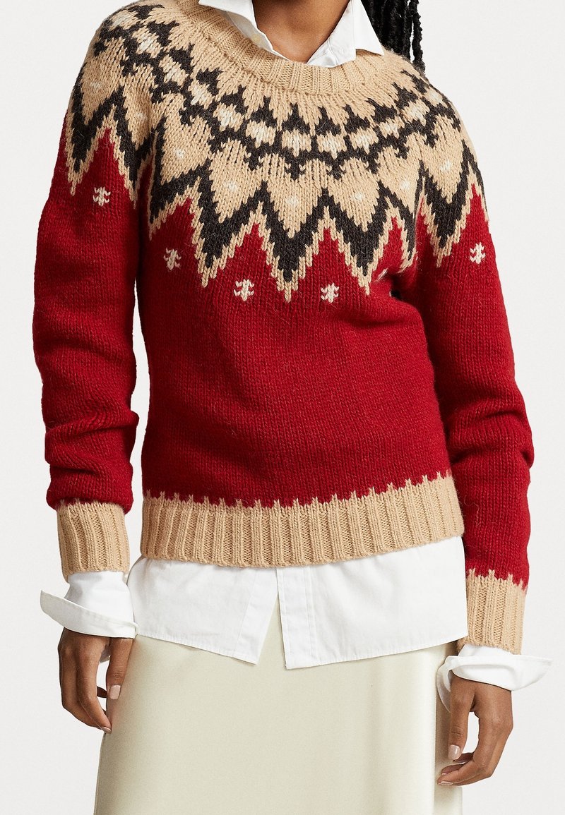 Pull rouge en tricot avec un motif jacquard beige et noir, col rond, poignets et ourlet côtelés. Chemise blanche à col portée en dessous.