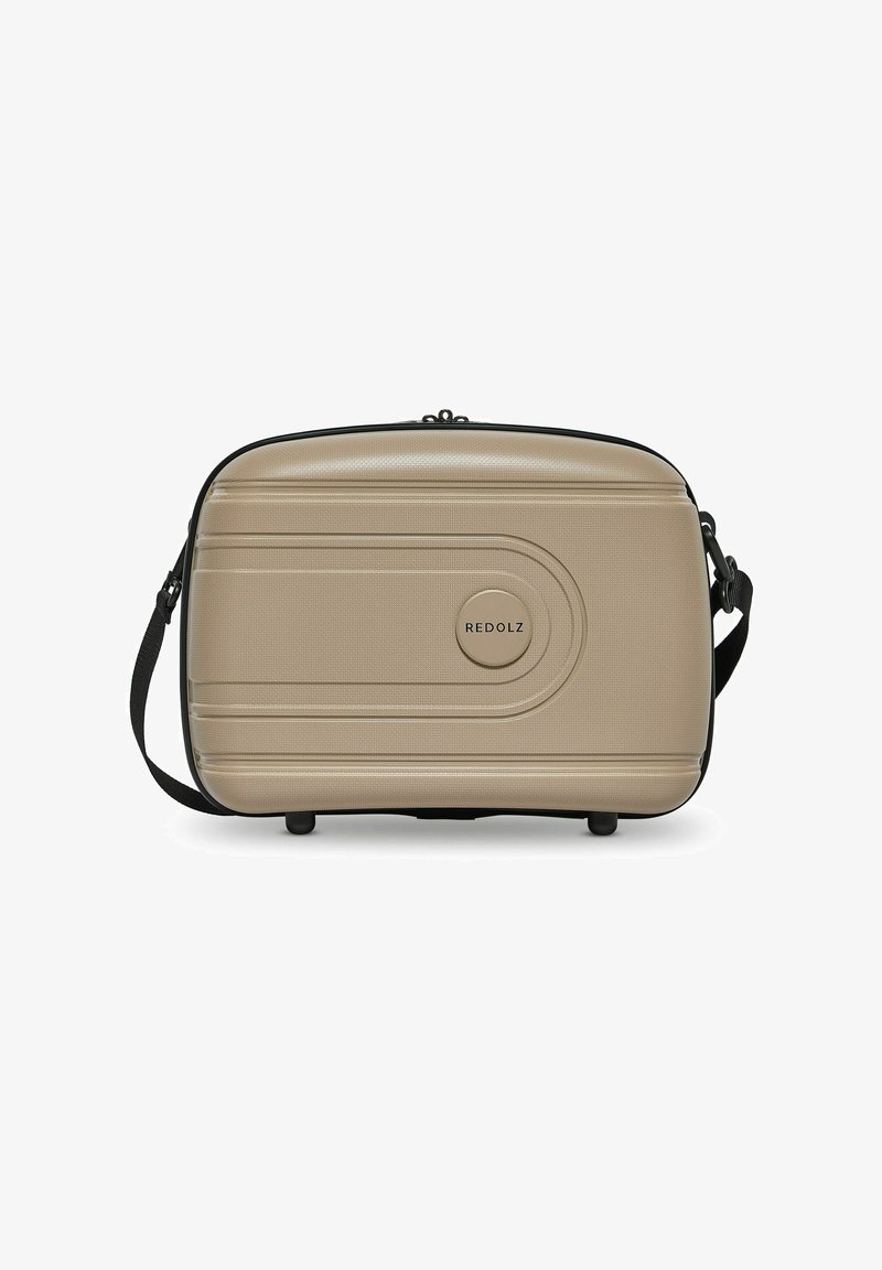 Beige rechthoekige tas met een gestructureerde afwerking, een ronde logo, een zwarte rits en een verstelbare schouderband. Voorzien van vier zwarte voeten aan de onderkant.