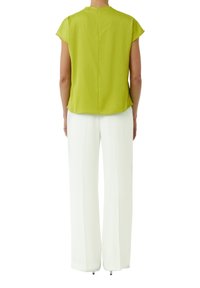 Jasnozielona bluzka krótki rękaw o prostym kroju i zamek z tyłu, w połączeniu z białymi, szerokimi spodniami. Gładki materiał i minimalistyczny design.