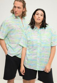 Kortærmede, knap-up skjorter i pastelfarver med abstrakte mønstre. Bæres med sorte shorts, der viser en afslappet pasform og letvægtsstof.
