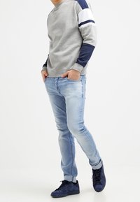 Grå sweatshirt med marinblå och vita randiga axlar, kombinerad med ljusblå slim-fit jeans och mörkblå sneakers.