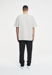 Helles graues, oversized T-Shirt mit kurzen Ärmeln, aus Baumwollmischgewebe, entspannte Passform. Getragen mit schwarzen Hosen und weißen Turnschuhen.