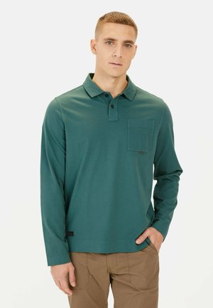 Langärmliges Polohemd in tiefem Teal, aus weichem Stoff. Verfügt über einen Kragen, eine Brusttasche und ein Etikett am unteren Saum.