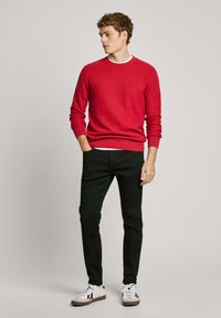 Red knitted sweater, black slim-fit pants, and white sneakers with black accents. The sweater features a round neck and ribbed cuffs.