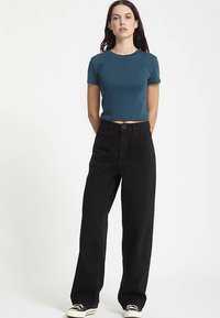 Teal cropped T-shirt with short sleeves, paired with loose-fitting black denim pants and black sneakers. Simple design with no visible patterns.
