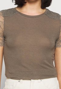 T-shirt marrone a coste con maniche in pizzo corto, scollatura rotonda e design aderente. Tessuto morbido con delicati dettagli in pizzo sulle spalle.