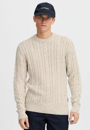 Helle beige Strickpulli mit langen Ärmeln, Rundhalsausschnitt und gerippten Bündchen und Saum. Kombiniert mit dunkelblauen Jeans und einer marineblauen Mütze.