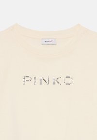 Cream cotton t-shirt with round neckline featuring "PINKO" in metallic decorative detail. Smooth texture, casual design.