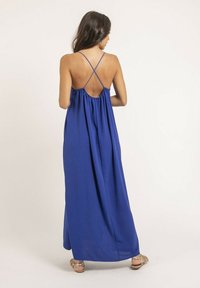 Robe maxi bleue avec une silhouette ample, dotée de bretelles croisées et d'un dos ouvert. Texture de tissu lisse et léger.