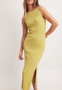 Robe sans manches jaune côtelée avec un col montant et une fente latérale, confectionnée dans un matériau texturé, ajustée près du corps.