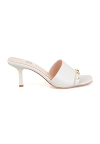 Mules à talons en cuir blanc avec un design épuré, bout ouvert, couture discrète et accents en pyramide dorée sur la bande supérieure.