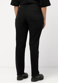 Pantalones vaqueros negros de mezclilla con un diseño de pierna recta, que cuentan con dos bolsillos traseros y una textura suave. Llevados con zapatos de plataforma negros.