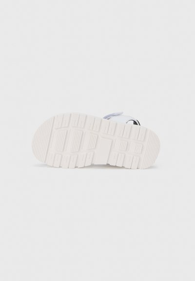 Λευκή σόλα αθλητικού παπουτσιού με υφή από καουτσούκ που διαθέτει ραβδωτό σχέδιο και ορθογώνιες λεπτομέρειες, προσφέροντας πρόσφυση και ανθεκτικότητα.