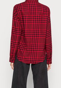 Red and black plaid shirt made of textured fabric, featuring a buttoned cuff and a straight back yoke design.