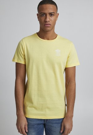 Gul bomulds T-shirt med rund hals, korte ærmer og et lille hvidt grafisk design med palmer på venstre bryst.
