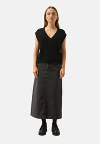 Svart stickad ärmlös topp med V-ringning, i kombination med en lång, mörkgrå denimkjol. Kraftiga svarta plattformsskor fulländar looken.