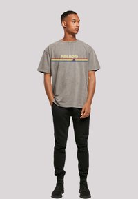 Gray oversized t-shirt with "PINK FLOYD" in yellow and rainbow stripes, paired with black sweatpants and black sneakers.