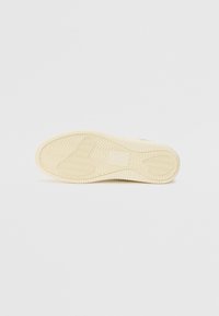 Textured rubber sneaker sole in cream, featuring a zigzag tread pattern and a rounded toe. Smooth edges and minimal branding visible.