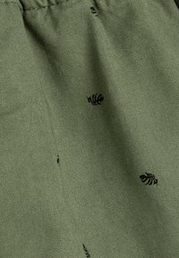 Groene stof met een gestructureerde afwerking, met kleine zwarte bladvormen die verspreid zijn over de stof. Zacht en duurzaam materiaal.
