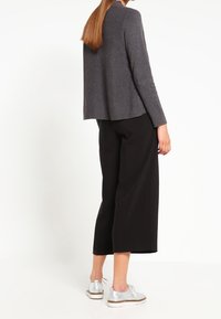 T-shirt gris à manches longues avec une coupe décontractée, associé à un pantalon large noir et des baskets argentées, vu de l'arrière.