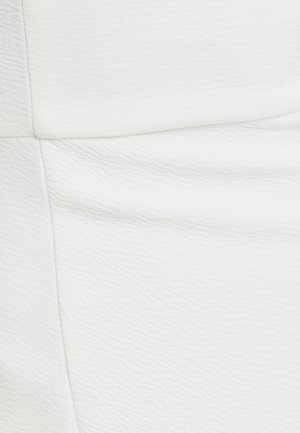 Tissu texturé blanc présentant des motifs géométriques en relief, avec des sections lisses et légèrement froissées, créant une profondeur visuelle et de l'intérêt.