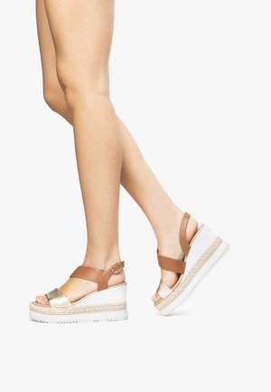 Sandali con zeppa con piattaforma bianca e texture intrecciata, dotati di cinturino in pelle marrone e fascia anteriore in metallo dorato. Fibbia regolabile alla caviglia.