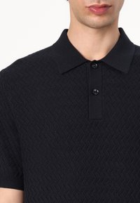 Svart polo skjorte med strukturert herringbone-mønster, tre-knappers placket, korte ermer og krage.