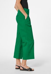 Groene wijde broek met hoge taille, zijzakken en een gladde textuur, gecombineerd met zwarte sandalen met een bandjesontwerp.